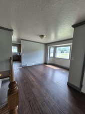 Unfurnished living room featuring plenty of natural light, dark wood-style flooring, a textured ceiling, and crown molding