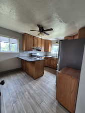 Kitchen featuring appliances with stainless steel finishes, a peninsula, brown cabinets, plenty of natural light, and a textured ceiling