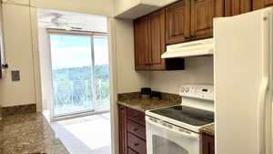 Kitchen with white appliances, carpet flooring, under cabinet range hood, dark countertops, and ceiling fan