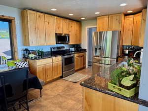 Kitchen featuring stainless steel appliances, dark stone counters, recessed lighting, light brown cabinets, and light tile patterned floors