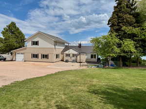 View of home with a front yard, board and batten siding, metal roof, a chimney, and gravel driveway