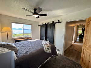 Bedroom with lake view, featuring a barn door, a ceiling fan