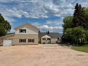 Modern farmhouse featuring board and batten siding, gravel driveway, and a garage