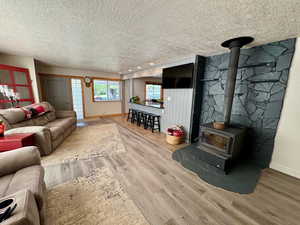 Living room featuring a textured ceiling, a wood stove, and wood-style finished floors