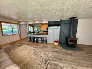 Living room to kitchen bar featuring wood-style finished floors, recessed lighting, and a wood stove