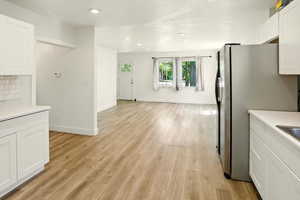 Kitchen with stainless steel fridge with ice dispenser, white cabinets, light countertops, light wood-style floors, and recessed lighting