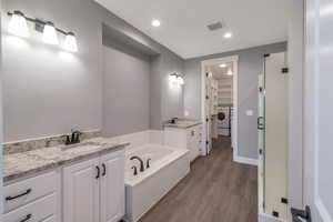 Bathroom with washer / dryer, a walk in closet, vanity, a bath, and wood finished floors