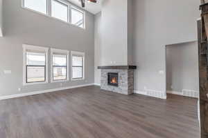 Unfurnished living room with a towering ceiling, a fireplace, a ceiling fan, and dark wood-type flooring