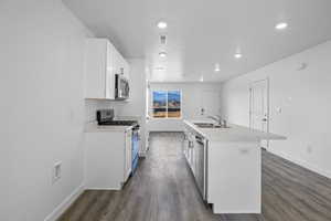 Kitchen featuring stainless steel appliances, an island with sink, white cabinets, light countertops, and dark wood finished floors