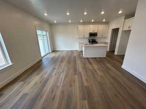 Kitchen featuring stainless steel microwave, a center island with sink, white cabinets, open floor plan, and recessed lighting