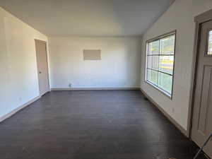 Unfurnished room featuring vaulted ceiling, dark wood-style flooring, and a textured ceiling