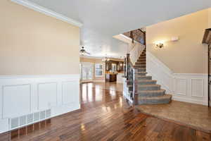 Staircase featuring ornamental molding, a chandelier, wood-type flooring, a decorative wall, and wainscoting