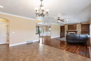 Living room featuring ceiling fan, a fireplace, ornamental molding, a chandelier, and built in features
