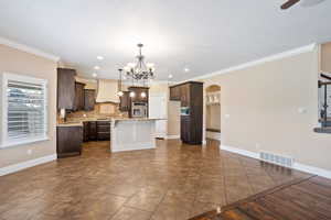 Kitchen featuring custom range hood, arched walkways, dark brown cabinets, a kitchen island, and crown molding