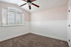 Carpeted bedroom featuring a wainscoted wall, ceiling fan, and lofted ceiling