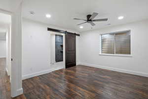 Unfurnished bedroom featuring a barn door, wood finished floors, recessed lighting, and ceiling fan