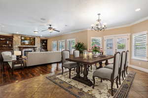 (Virtual Staging) Tiled dining space with a ceiling fan, ornamental molding, a stone fireplace, a chandelier, and built in features