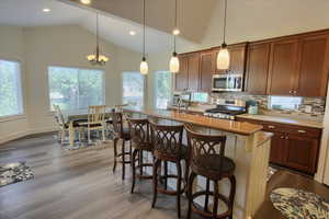 Kitchen featuring appliances with stainless steel finishes, dark wood-style flooring, vaulted ceiling, tasteful backsplash, and a kitchen bar