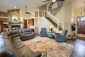 Living room with ceiling fan, high vaulted ceiling, stairway, wood-type flooring, and a fireplace