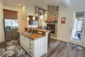Kitchen with appliances with stainless steel finishes, dark wood-type flooring, a breakfast bar, a stone fireplace, and dark stone countertops