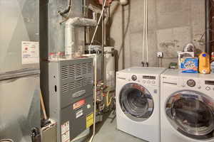Laundry area with washing machine and clothes dryer, strapped water heater, and heating unit
