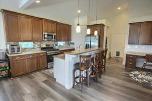 Kitchen featuring appliances with stainless steel finishes, a kitchen bar, backsplash, vaulted ceiling, and wood finished floors
