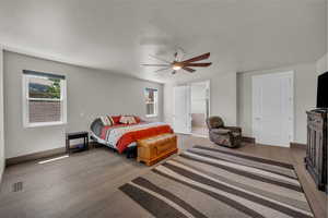 Bedroom with wood finished floors, multiple windows, ensuite bathroom, and ceiling fan
