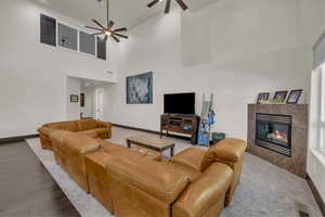 Living area featuring a ceiling fan, a high ceiling, a premium fireplace, and wood finished floors