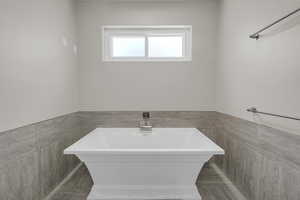 Bathroom featuring tile walls, a soaking tub, and a wainscoted wall