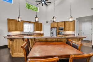 Kitchen featuring stainless steel appliances, a high ceiling, ceiling fan, brown cabinetry, and a breakfast bar area