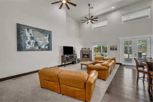Living room with a ceiling fan, a towering ceiling, a fireplace, wood-type flooring, and recessed lighting