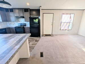 Kitchen featuring freestanding refrigerator, gas stove, tasteful backsplash, under cabinet range hood, and carpet flooring