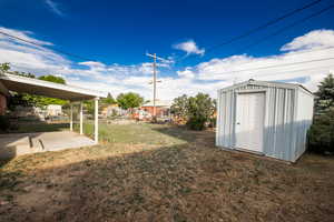 View of grassy yard featuring a storage shed and a patio