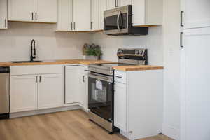 Kitchen featuring wooden counters, appliances with stainless steel finishes, decorative backsplash, light wood-style flooring, and white cabinets