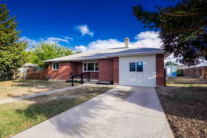 Ranch-style home featuring a storage unit, a chimney, brick siding, driveway, and board and batten siding