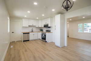 Kitchen featuring stainless steel appliances, light wood-style flooring, recessed lighting, white cabinetry, and wooden counters
