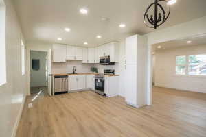 Kitchen featuring stainless steel appliances, a chandelier, light wood finished floors, recessed lighting, and white cabinetry