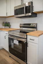 Kitchen featuring stainless steel appliances, butcher block counters, decorative backsplash, and light wood-style flooring