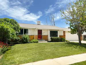 Ranch-style home with brick siding, an attached garage, a front yard, and a chimney