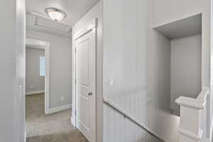 Hallway featuring an upstairs landing, attic access, and carpet