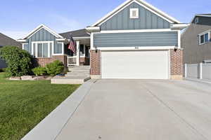 View of front facade featuring board and batten siding, driveway, a front yard, a garage, and brick siding