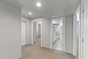 Hallway featuring light colored carpet, recessed lighting, and a textured ceiling