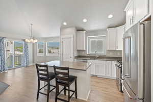Kitchen with stainless steel appliances, a chandelier, light wood-style floors, white cabinets, and recessed lighting