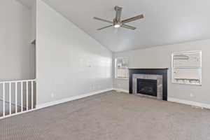 Unfurnished living room featuring a ceiling fan, carpet floors, a fireplace, and vaulted ceiling