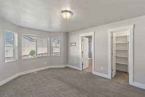 Unfurnished bedroom with a spacious closet, carpet flooring, a closet, ensuite bath, and a textured ceiling