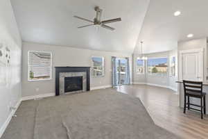 Unfurnished living room featuring a chandelier, a tiled fireplace, ceiling fan, wood finished floors, and vaulted ceiling