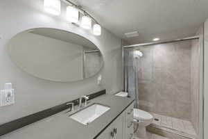 Full bath with a textured ceiling, vanity, and a stall shower