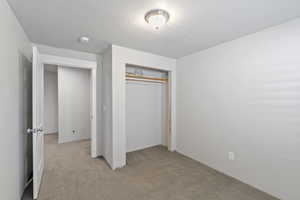 Unfurnished bedroom with light colored carpet, a closet, and a textured ceiling