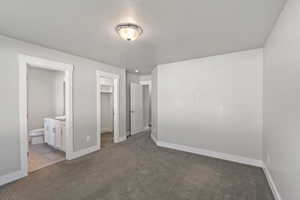 Unfurnished bedroom featuring a walk in closet, light colored carpet, ensuite bath, and a closet