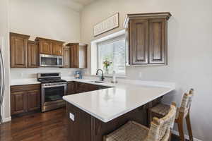 Kitchen featuring appliances with stainless steel finishes, a peninsula, a kitchen bar, dark wood-style floors, and light countertops